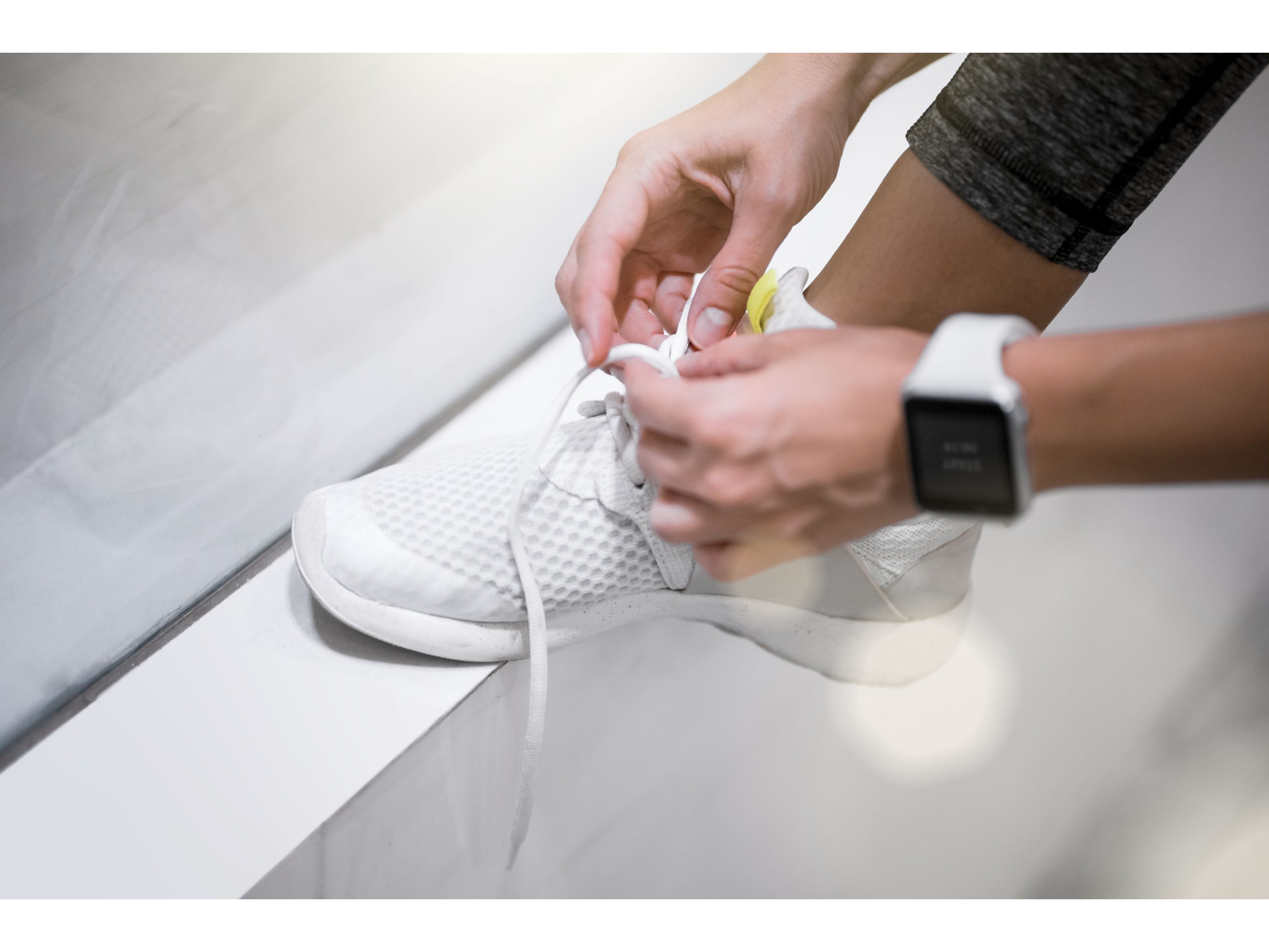 Focus on woman's hands with smart watch lace up her sneakers